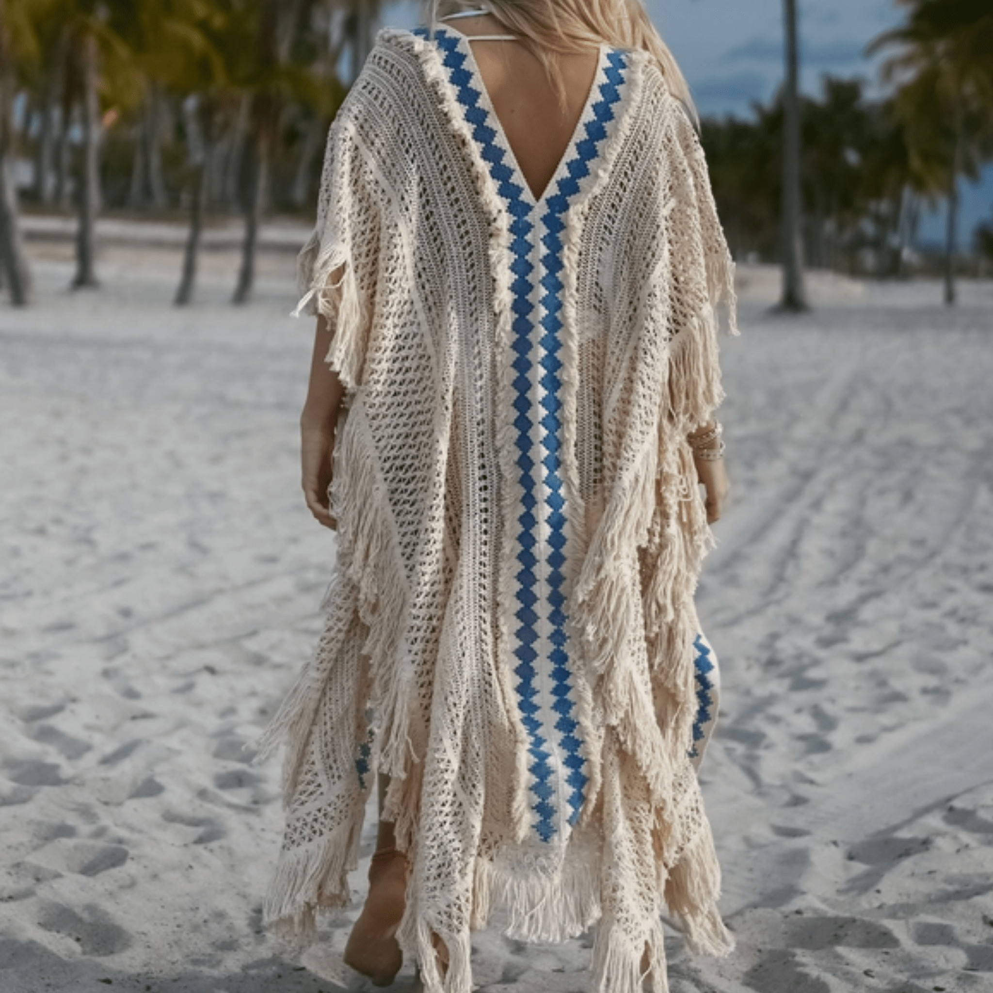 A bohemian knit kimono draped on a mannequin; made from soft, naturally dyed blue cotton with intricate knit patterns and delicate fringes. Lightweight and breathable, it blends comfort with artisanal elegance—perfect for beach lounging, festivals, or a resort-chic layered look.