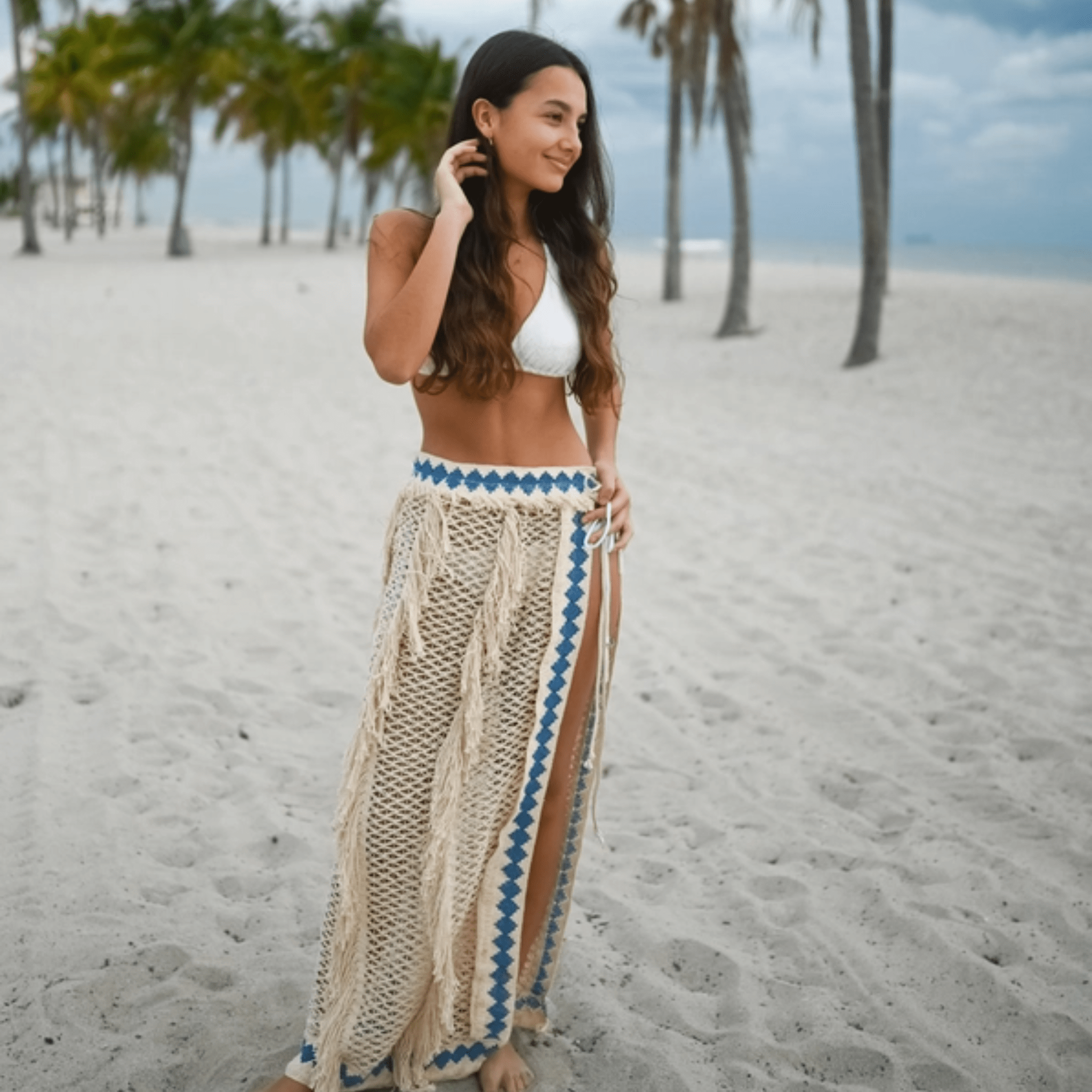 A lightweight resort knit pareo made of soft, breathable cotton, featuring a delicate knit pattern, natural fringes, and a blue embroidered border. Designed with a flattering tie-waist, this bohemian wrap moves gracefully—ideal for beach days or festival nights.